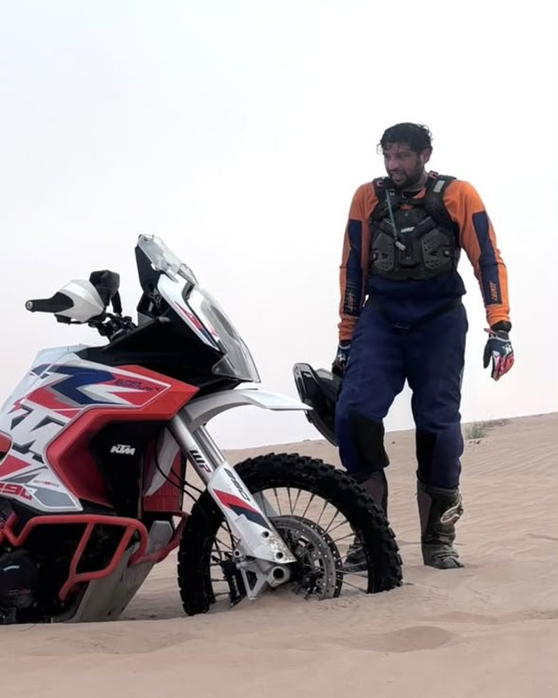 Suji standing next to his KTM, buried in the sand